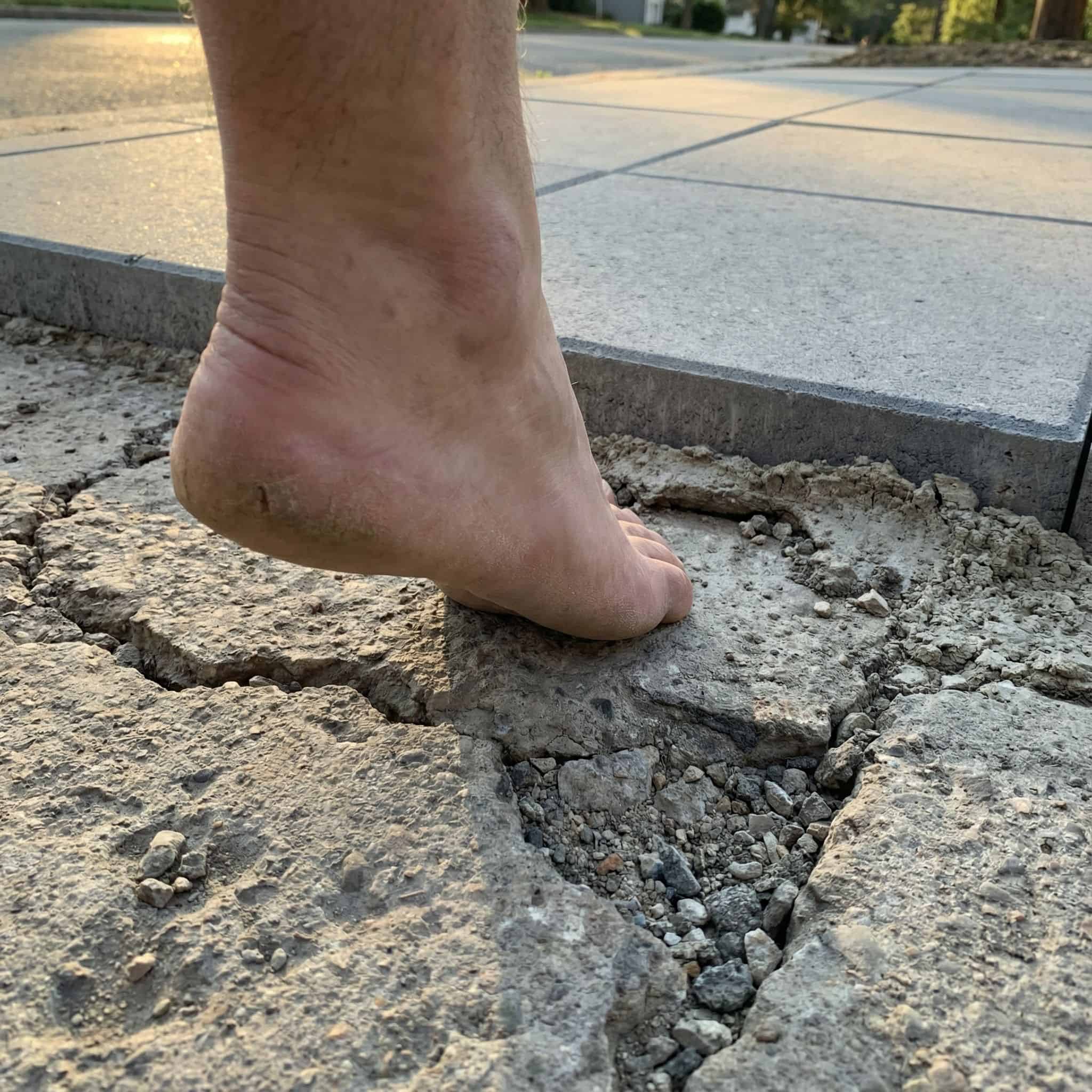 균열이 간 위험한 보도 위에 맨발이 망설이며 한 걸음 앞에는 깨끗한 안전한 보도가 보이는 모습이다.
